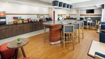 Un lobby moderno de hotel con una barra central, zonas de estar y una encimera de cocina con diversos servicios.