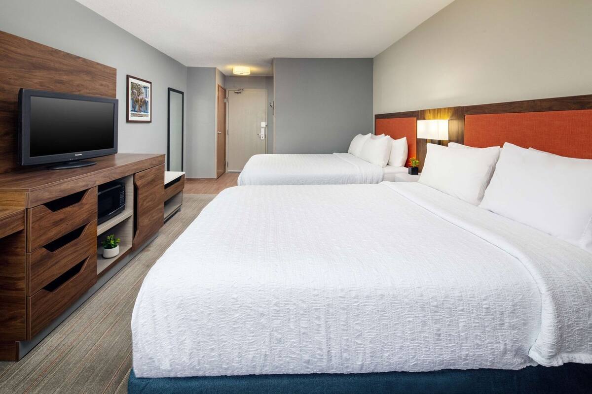 A hotel room with a bed, a TV, a wooden dresser, and a door.