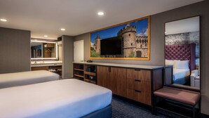 Une chambre d’hôtel avec deux lits, un grand miroir, un tableau représentant un château et un petit coin salon.