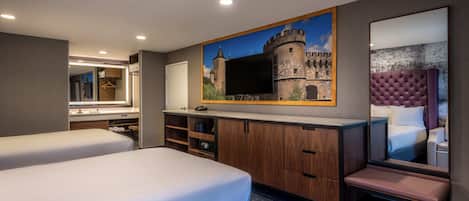 Habitación de hotel con dos camas, un espejo grande, un cuadro de un castillo y una pequeña zona de estar.
