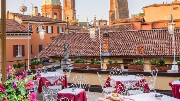 Une terrasse avec des tables préparées pour le petit-déjeuner, offrant une vue sur des bâtiments historiques et une tour.