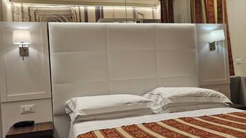 A hotel room with a large bed, a bedside table with a lamp, a power outlet, and a small desk with a remote control.