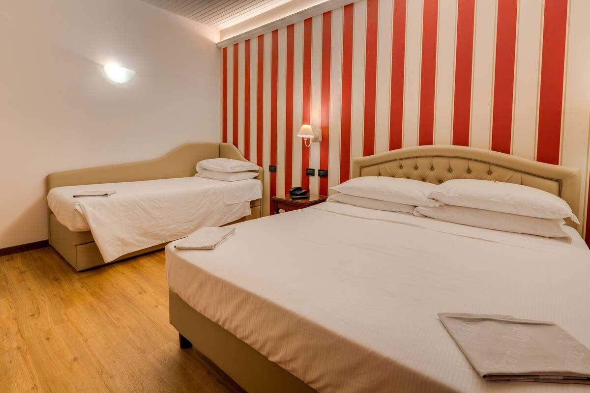 Une chambre d’hôtel avec deux lits, un plancher en bois, un mur à rayures et une table de chevet avec une lampe.