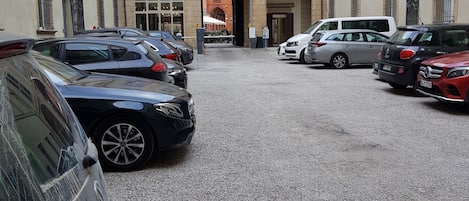 Un área de estacionamiento con varios coches aparcados frente a un edificio de ventanas arqueadas y un arco central.