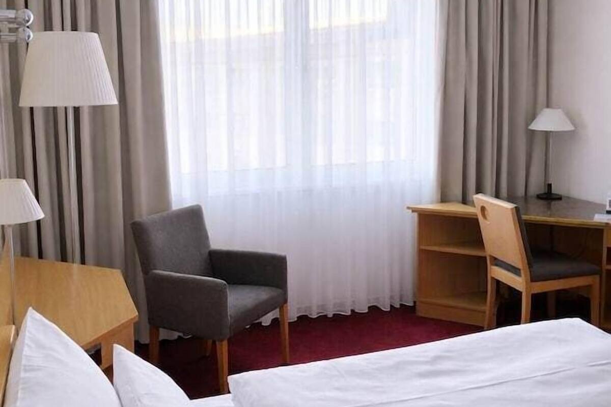 Een hotelkamer met een bed, twee stoelen, een bureau en een raam met gordijnen.