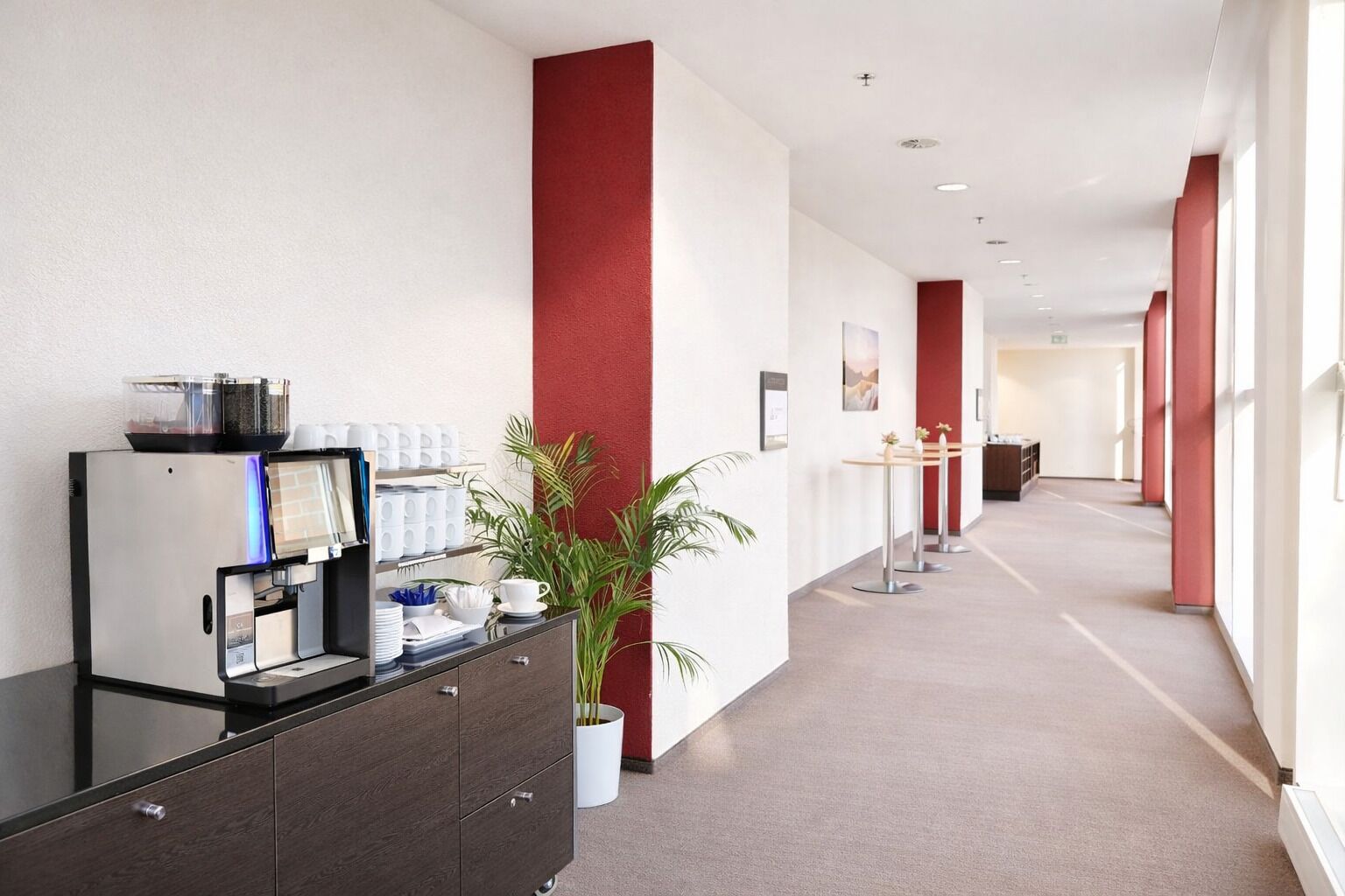 Un couloir d’hôtel avec un comptoir de réception, une machine à café et une plante en pot.