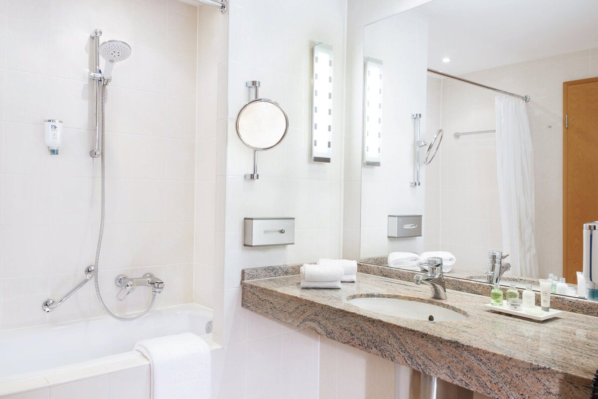A modern bathroom with a shower, a sink with a granite countertop, a mirror, and a towel rack.