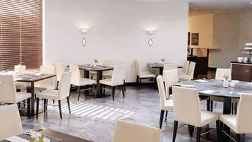 Um espaço de jantar de hotel moderno com mesas redondas, cadeiras bege e teto com claraboias.