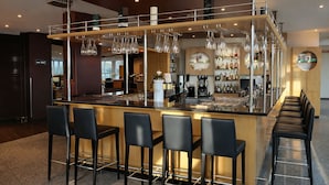 A modern bar area with a central island, bar stools, and a variety of bottles and glasses on shelves. - Hotel Dresden Neustadt (Dresden)