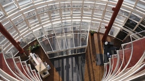 A high-ceiling atrium with a glass ceiling, a central staircase, and a seating area with tables and chairs. - Hotel Dresden Neustadt (Dresden)