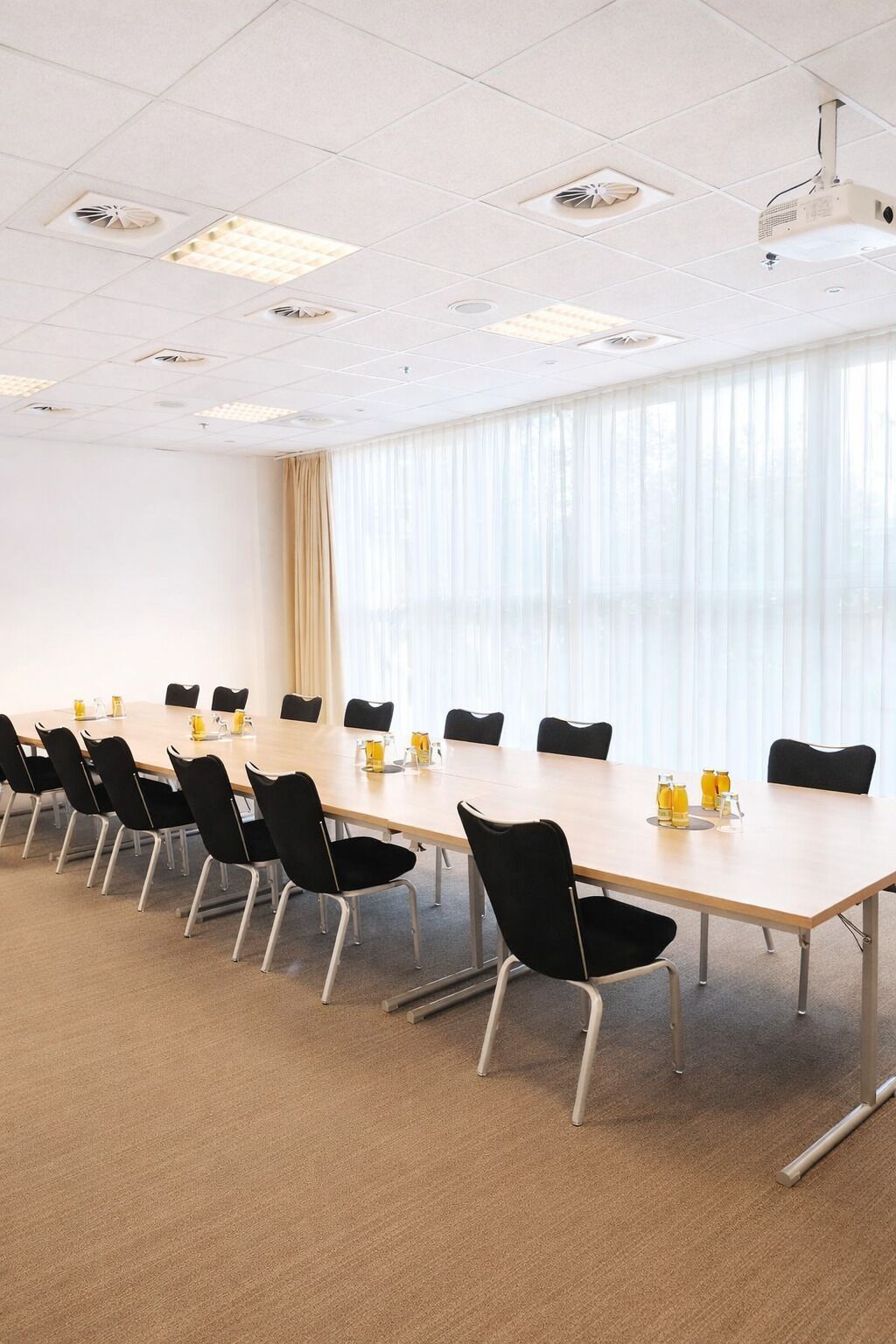Ein Konferenzraum mit einem langen Tisch, schwarzen Stühlen und einem großen Fenster mit Vorhängen.