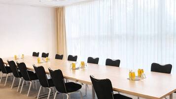 Ein Konferenzraum mit einem langen Tisch, schwarzen Stühlen und einem großen Fenster mit Vorhängen.