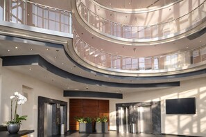 Ein mehrgeschossiges Atrium mit Glasgeländern, Aufzügen und Topfpflanzen.
