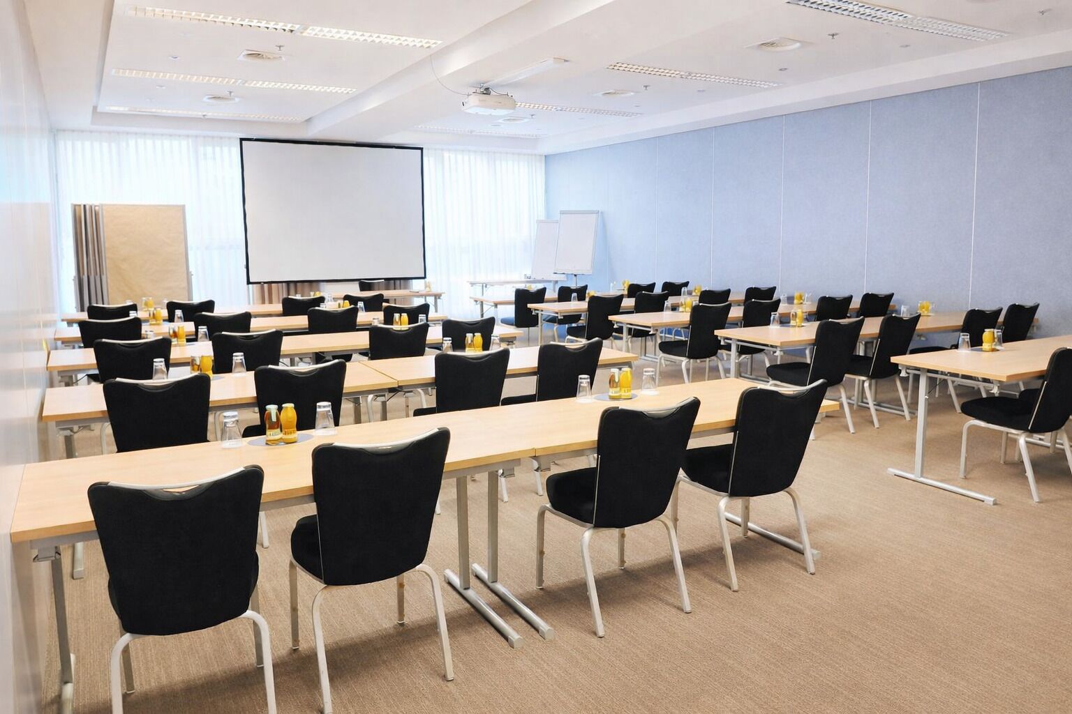 Ein Konferenzraum mit mehreren Tischen, Stühlen, einer Projektorleinwand und einer Whiteboard-Tafel.