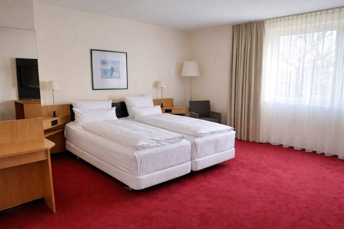 Ett hotellrum med två sängar, ett skrivbord, en stol, en TV och ett fönster med gardiner.