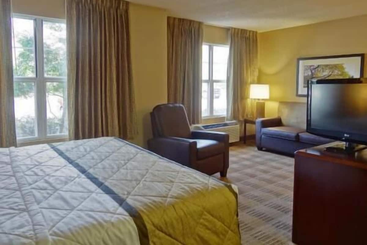 Ein Hotelzimmer mit Bett, Schreibtisch, Stuhl, Fernseher und einem Fenster mit Vorhängen.