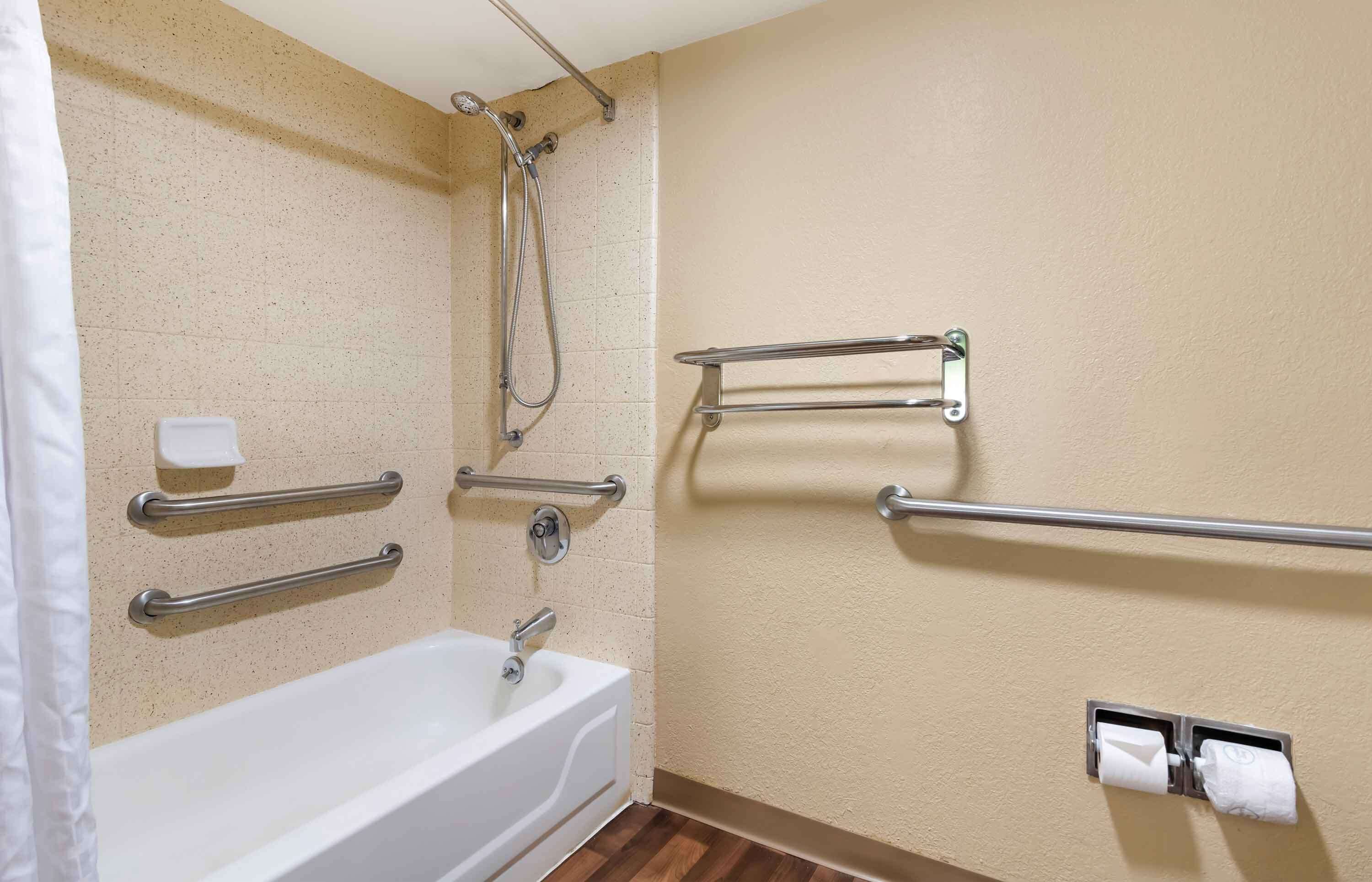 A bathroom with a bathtub, a shower, and handrails.