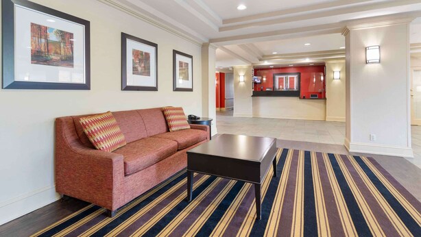 Un vestíbulo amplio con un sofá rojo, una mesa de centro negra y alfombra a rayas. Hay cuadros enmarcados en la pared y una zona de recepción al fondo.