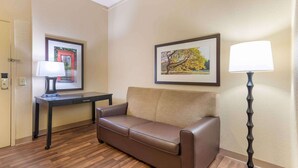 Una habitación de hotel con un sofá de cuero marrón, un escritorio pequeño con una lámpara y dos cuadros en la pared.