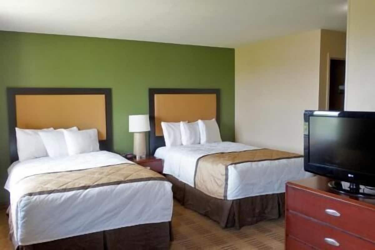 Ein Hotelzimmer mit zwei Betten, einem Fernseher und einem Schminktisch.