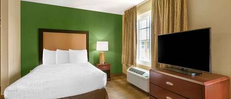 A hotel room with a large bed, a flat-screen TV, a nightstand, a lamp, and a window with curtains.