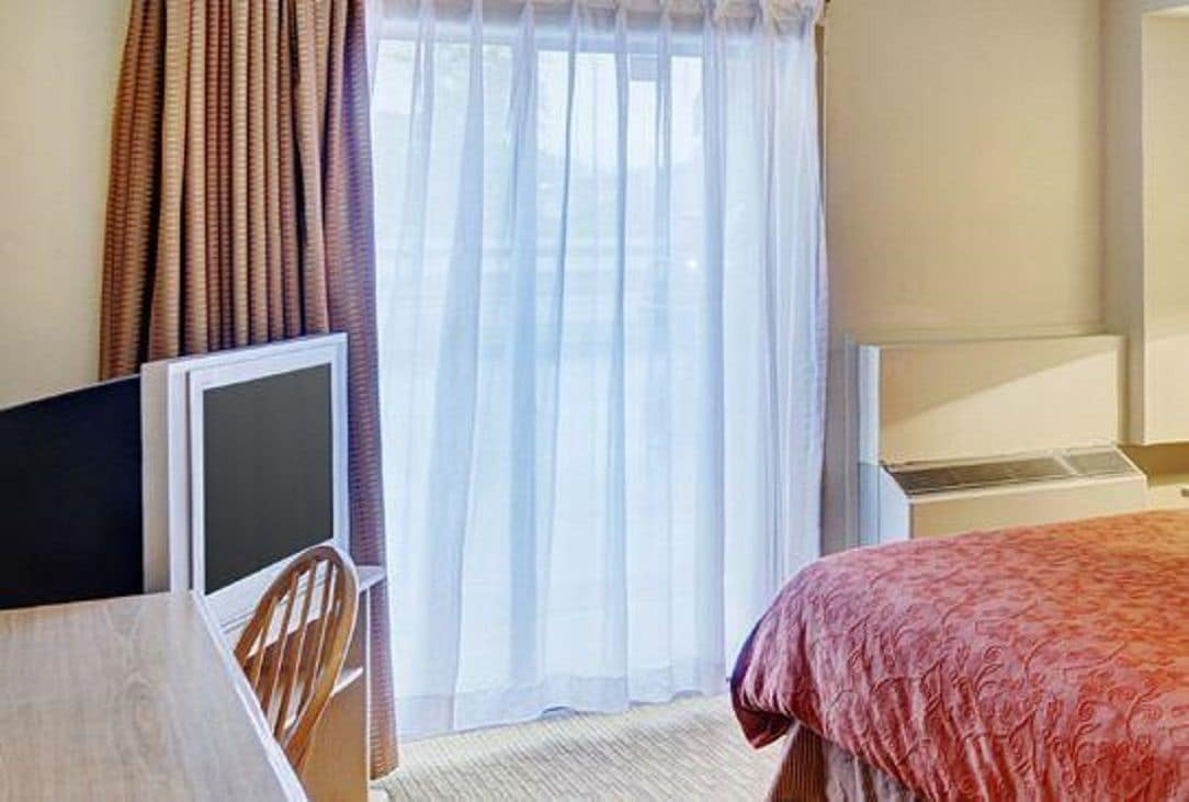 Una habitación de hotel con una cama, un escritorio con ordenador y una ventana con cortinas.