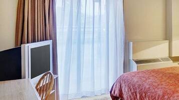 Una habitación de hotel con una cama, un escritorio con ordenador y una ventana con cortinas.