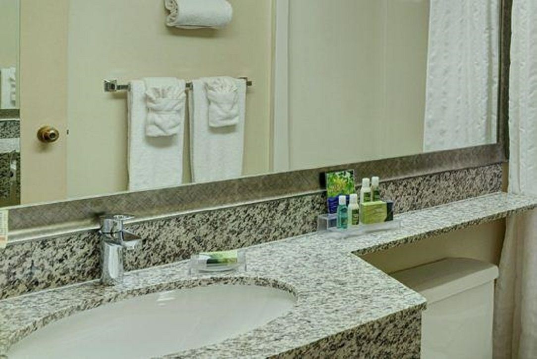 A bathroom with a granite countertop, a sink, and a mirror. There are two white towels hanging on a towel rack.