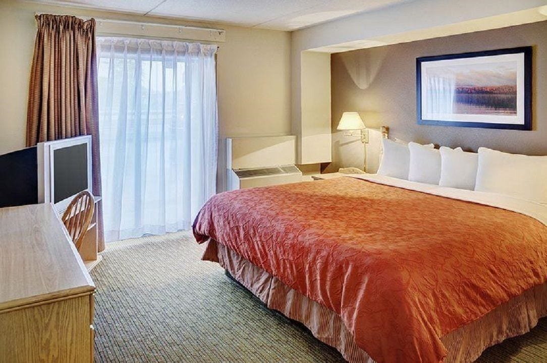 A hotel room with a large bed, a desk, a chair, a TV, a lamp, and a framed picture on the wall.