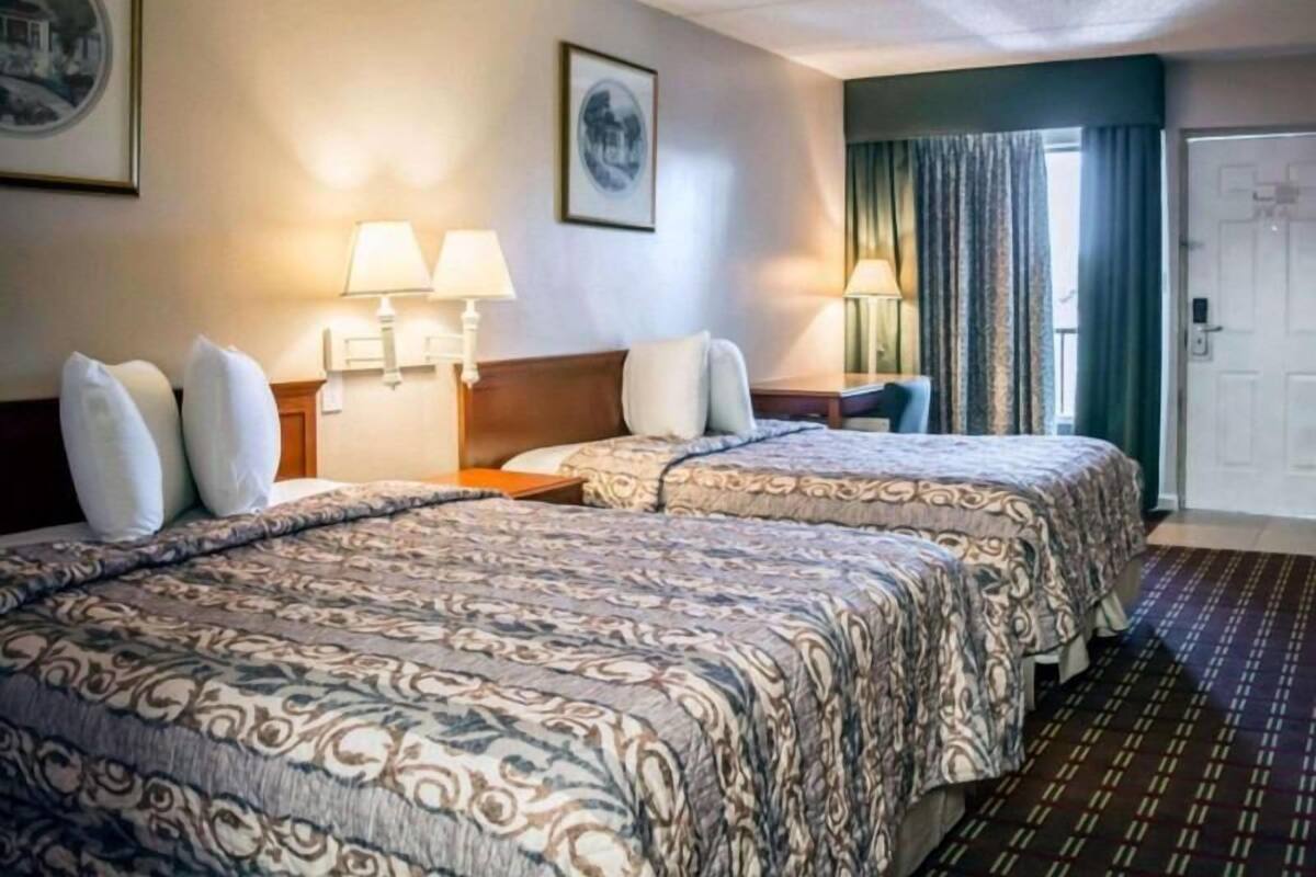 A hotel room with two beds, a desk, a chair, a lamp, and a door.