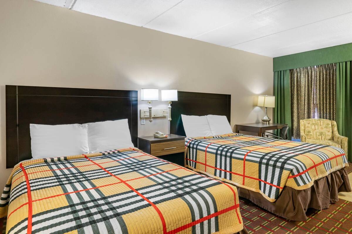 A hotel room with two beds, a nightstand, a chair, and a desk with a lamp.
