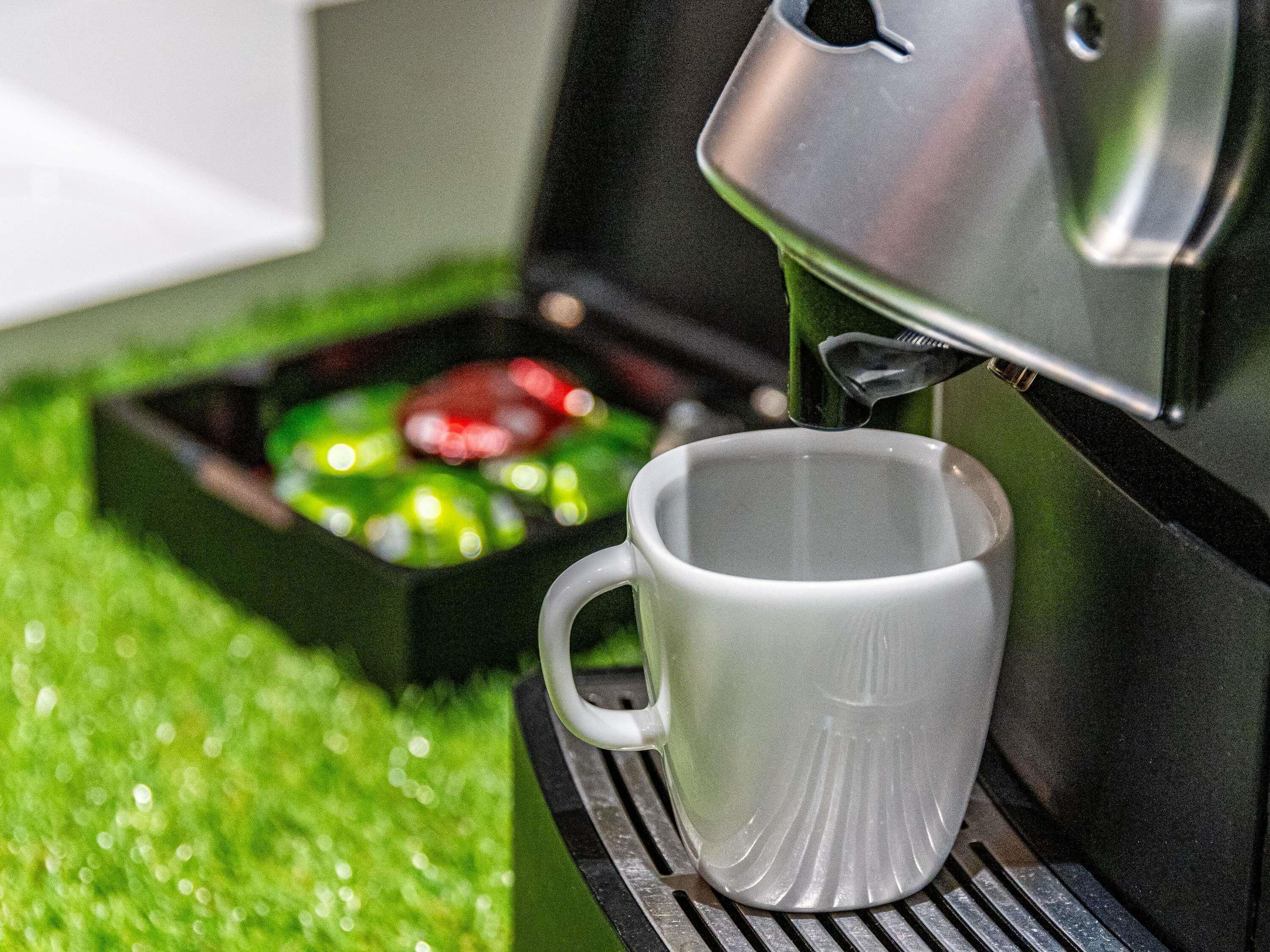 Une machine à café verse du café dans une tasse blanche posée sur un plateau.