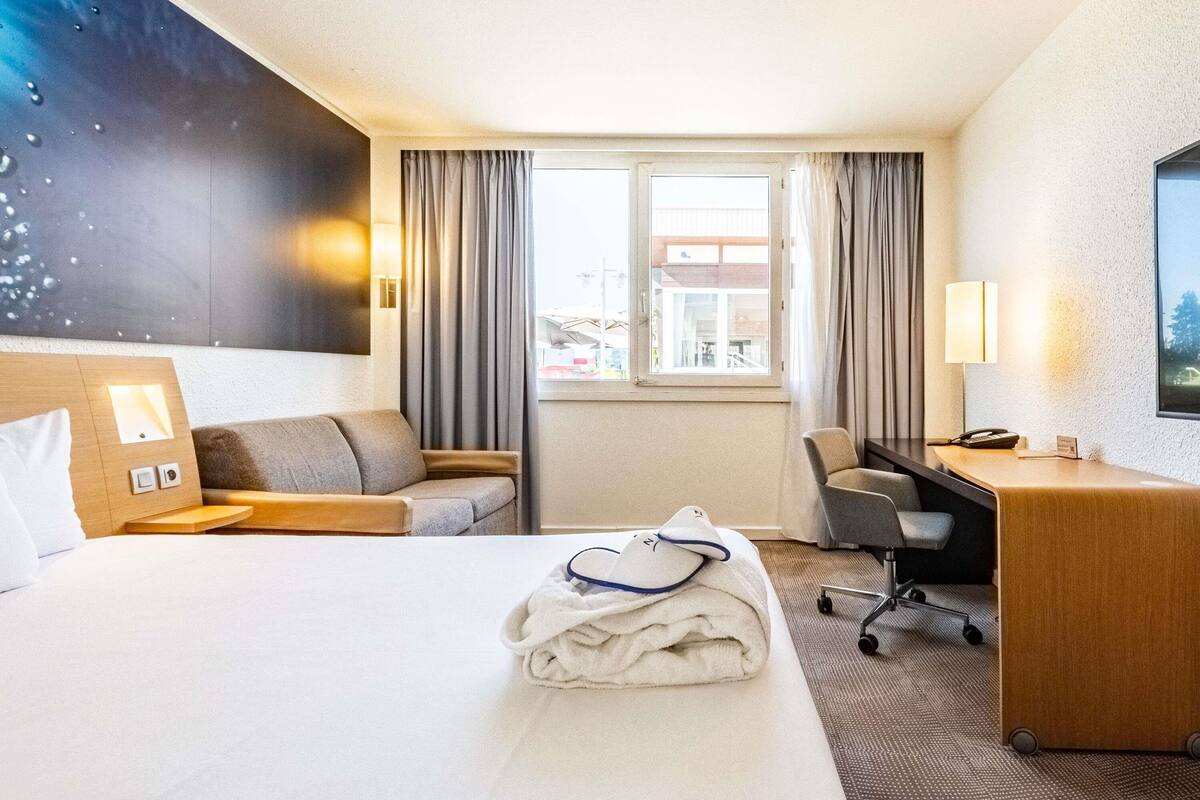 A hotel room with a bed, a desk, a chair, a window, and a view of the outside.