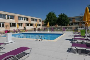 Una piscina al aire libre, sombrillas, sillones reclinables de piscina