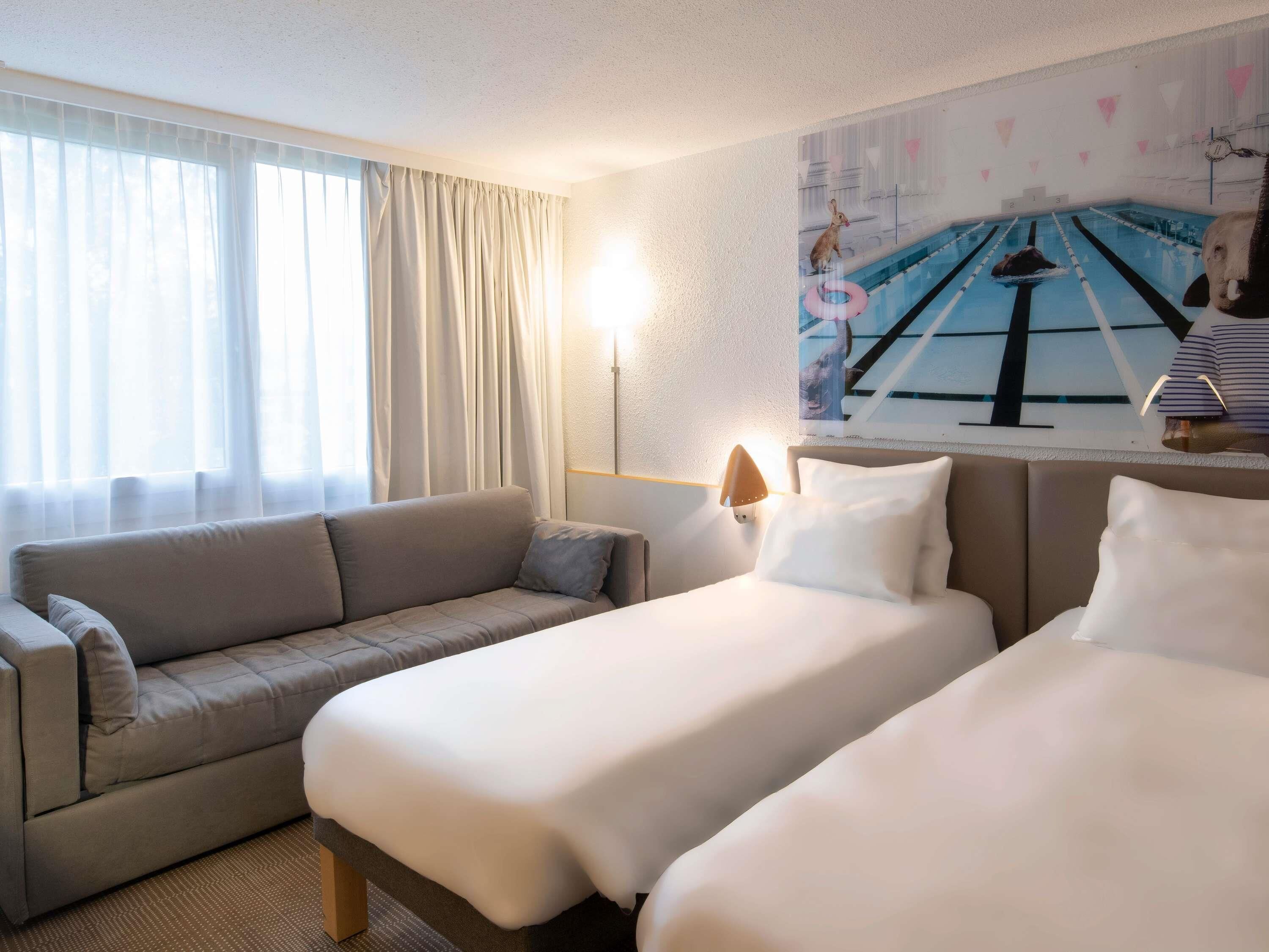 Habitación de hotel con sofá, dos camas, una lámpara y un cartel con una piscina.