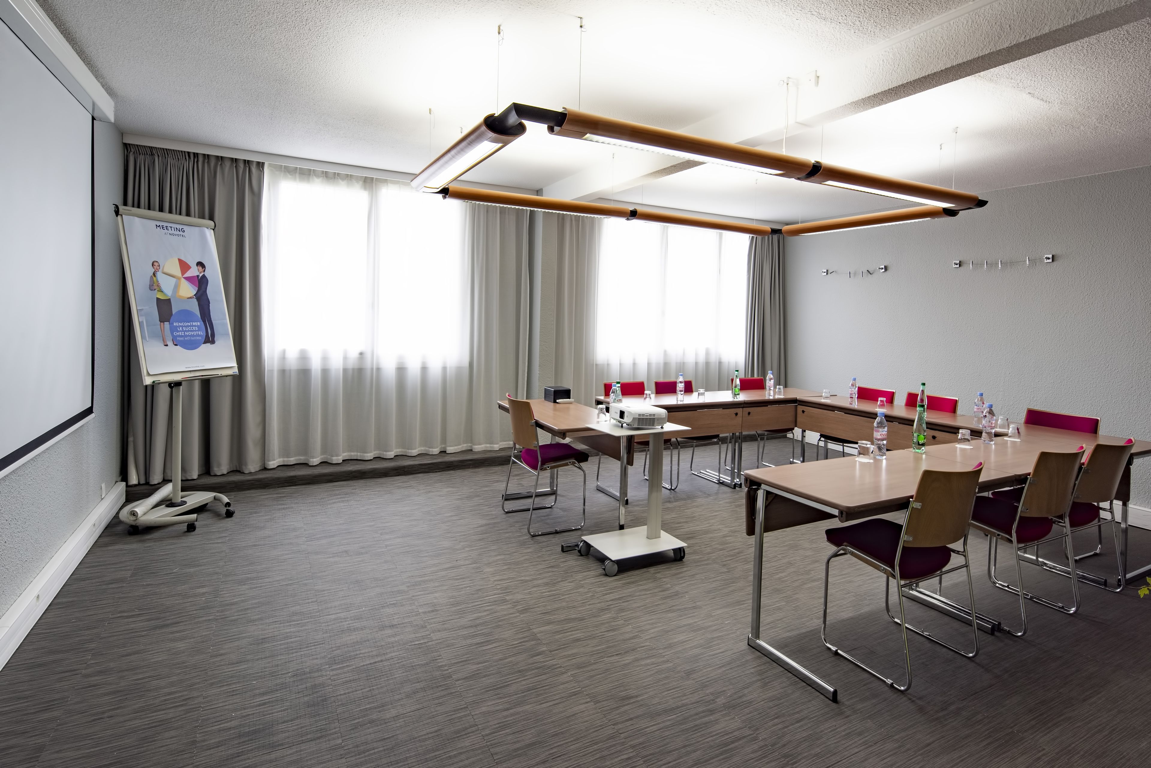 Une salle de conférence équipée d’une grande table, de chaises, d’un projecteur et d’un écran affichant l’ordre du jour de la réunion.