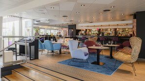 A modern bar area with seating, a piano, and a staircase.