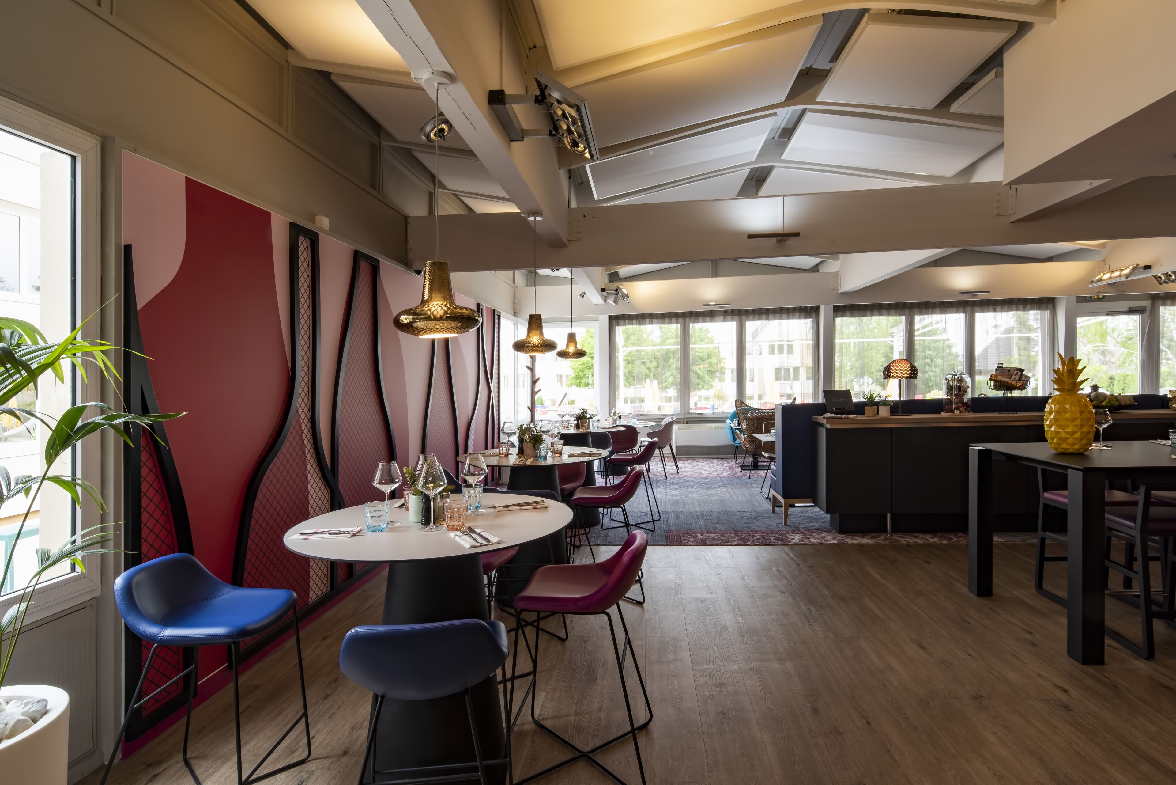 Un espace repas moderne avec des tables rondes, des chaises bleues et rouges, et des luminaires suspendus.