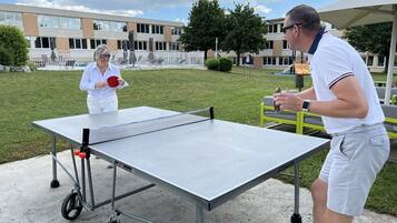 Mesa de ping pong al aire libre instalada en un área verde con un edificio al fondo.