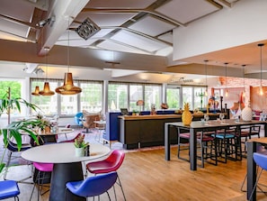 A modern interior with a dining area, seating, and a bar. - Novotel Dijon Sud (Marsannay-la-Cote)
