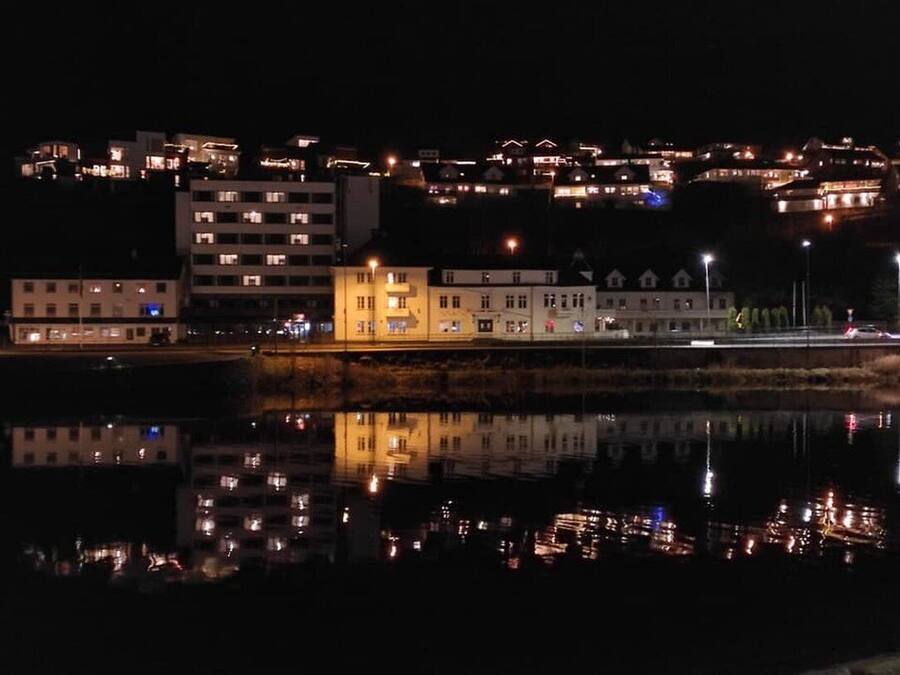 Vista nocturna de una zona costera con edificios reflejados en el agua.
