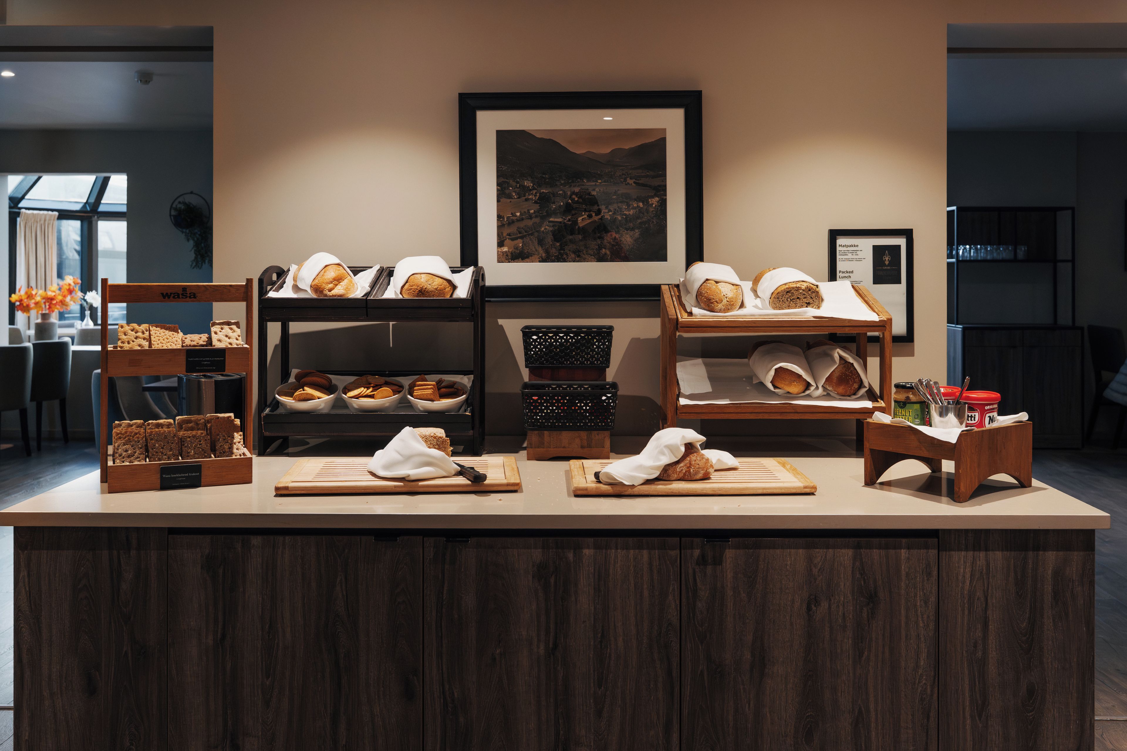 Mostrador de panadería con diversos panes y pasteles, un cuadro con paisaje y un panel con la carta.