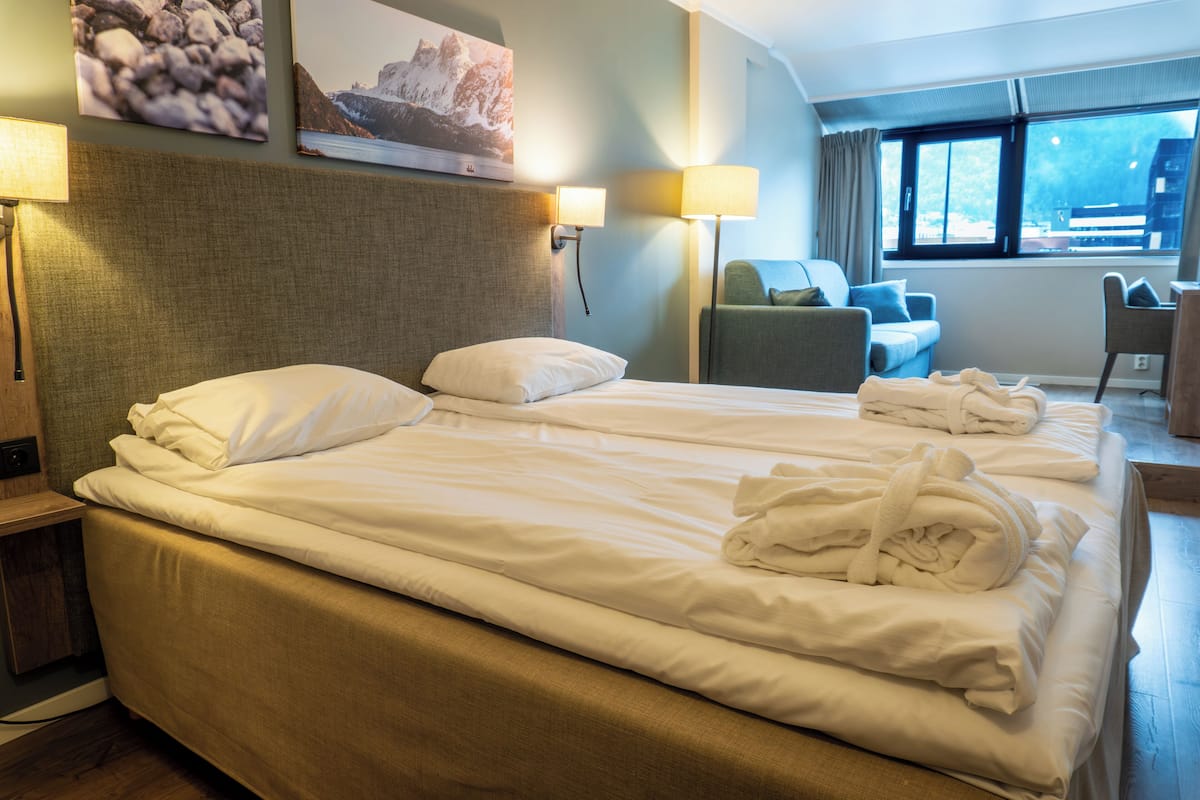 Habitación de hotel con cama, dos lámparas de pared, una silla, un escritorio y una ventana con cortinas.