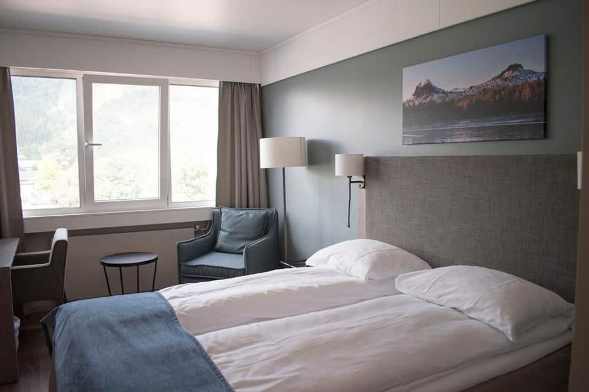 Una habitación de hotel con una cama, un escritorio, una silla y una ventana.