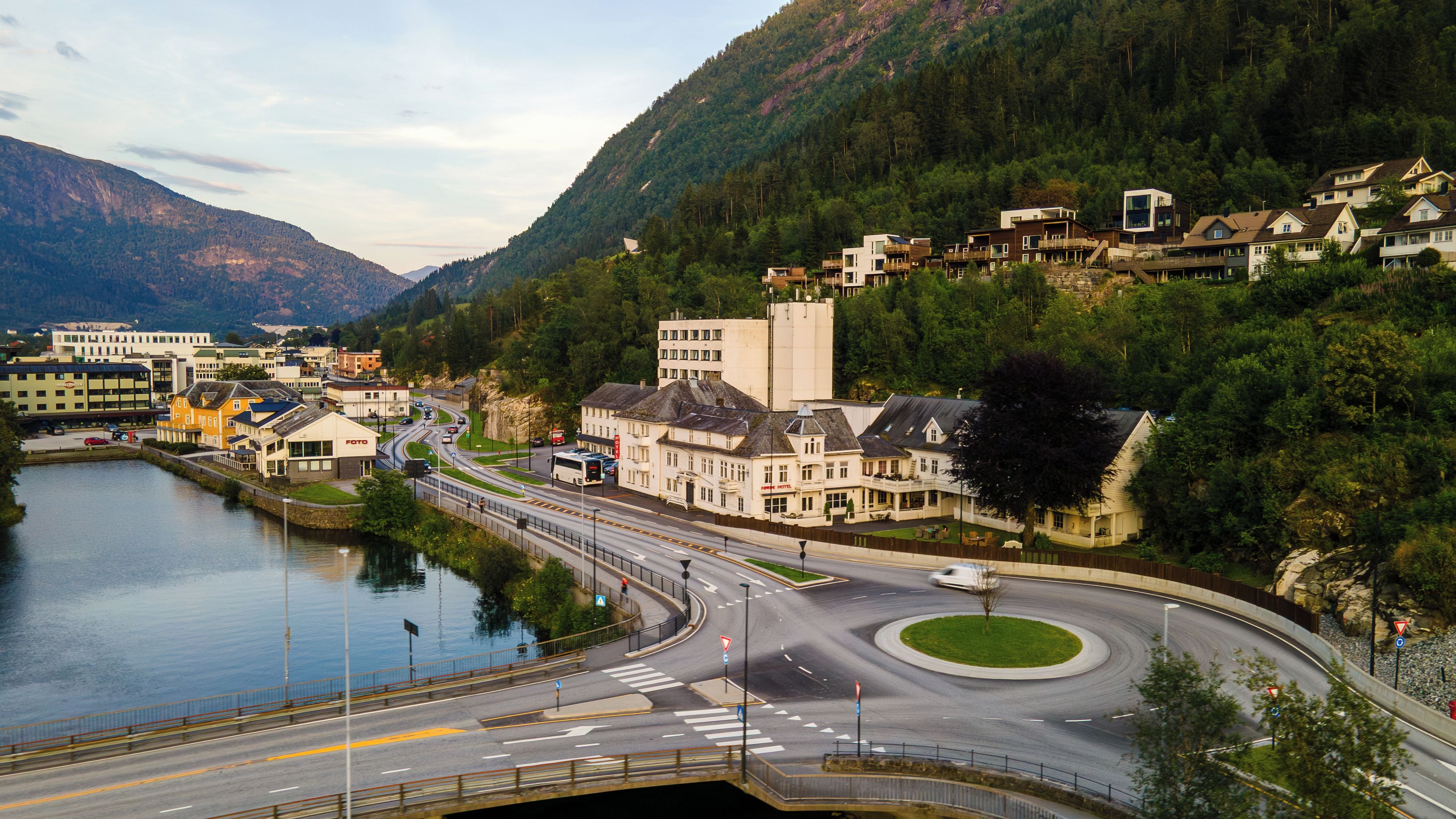 A riverside town with a hotel, a roundabout, and a mountain backdrop.