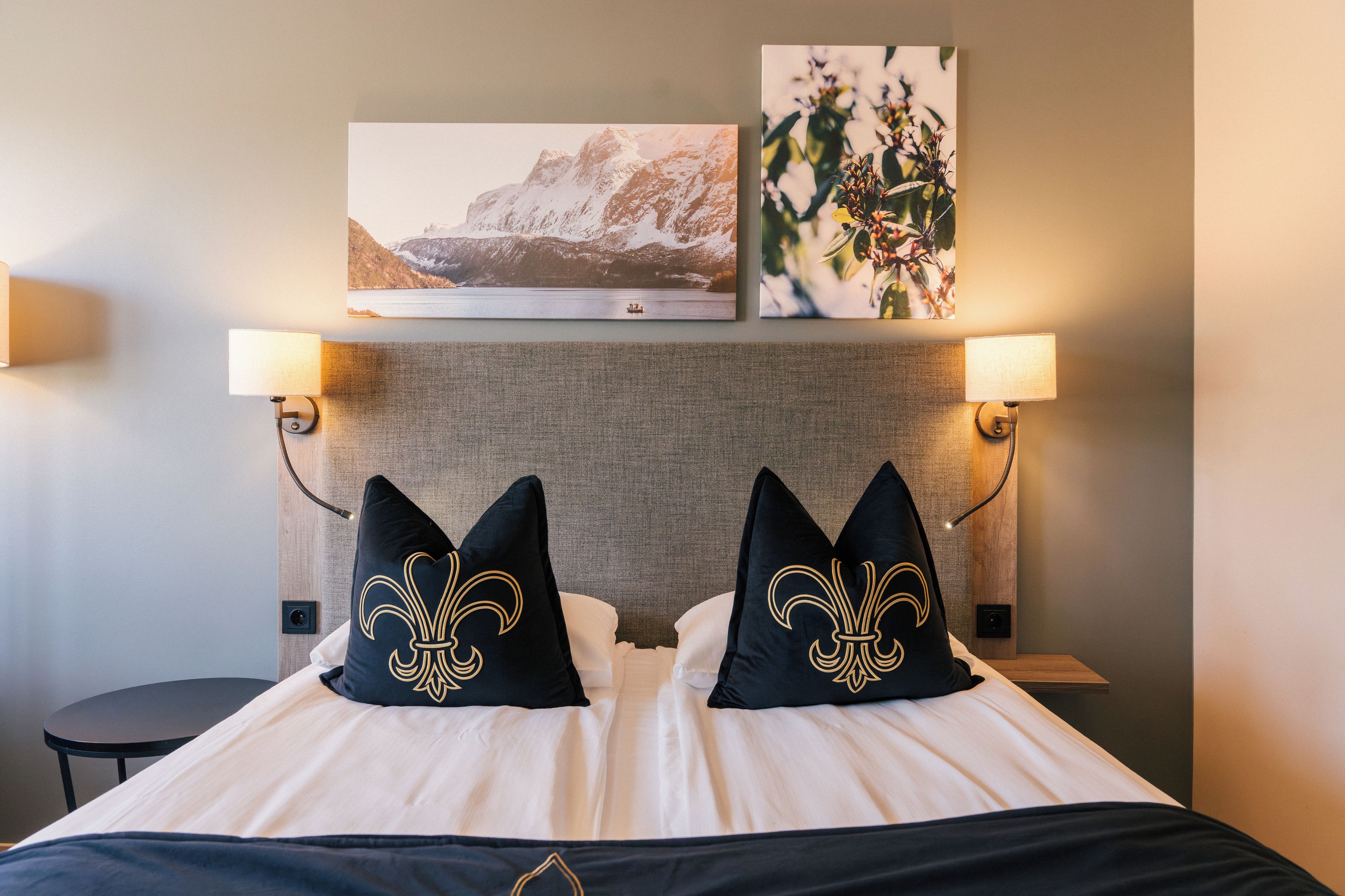 A hotel room with a bed, two wall-mounted lamps, a headboard, and two framed pictures.