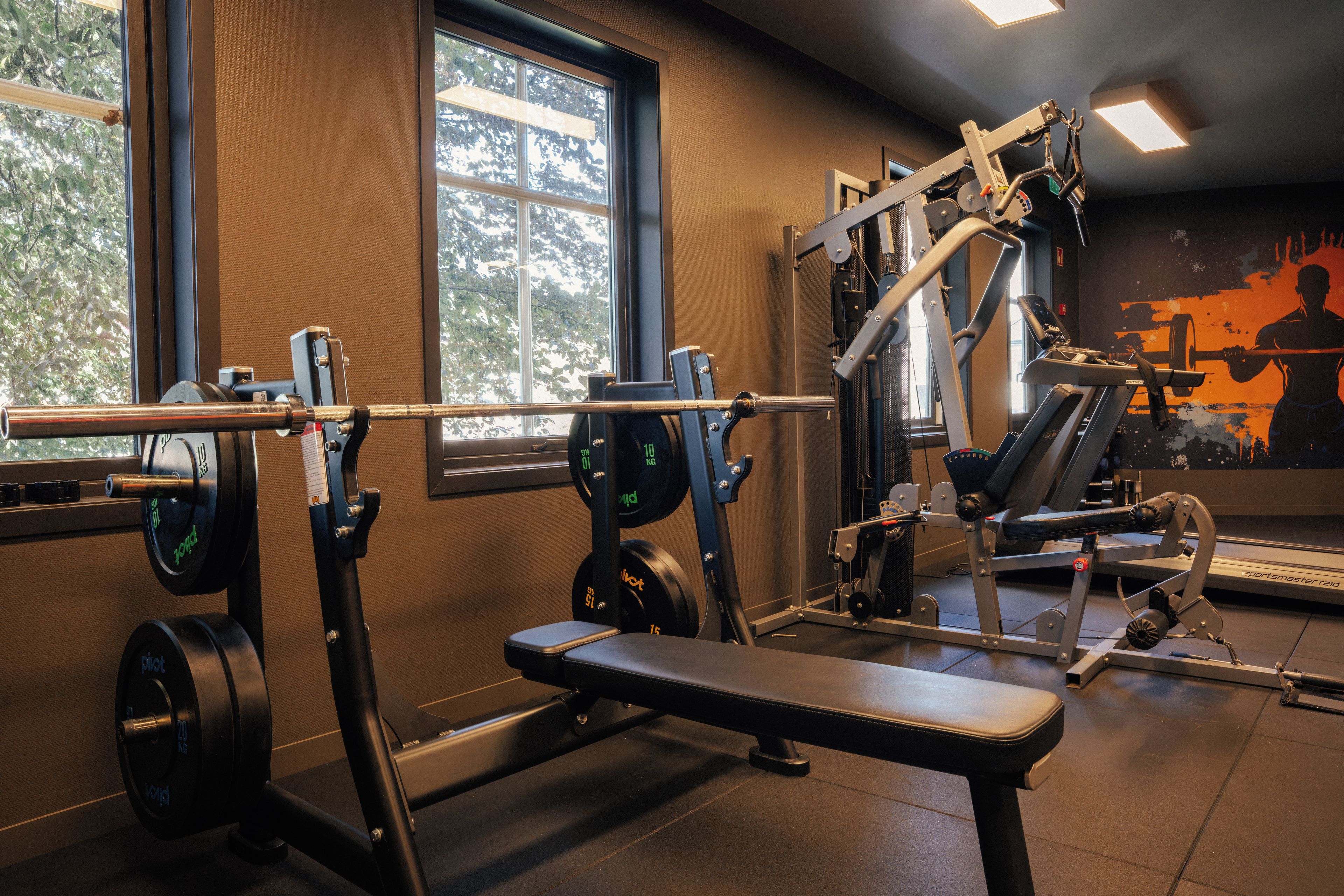 Een sportschool met diverse fitnessapparaten, waaronder een bank en gewichtsafzetmachines.