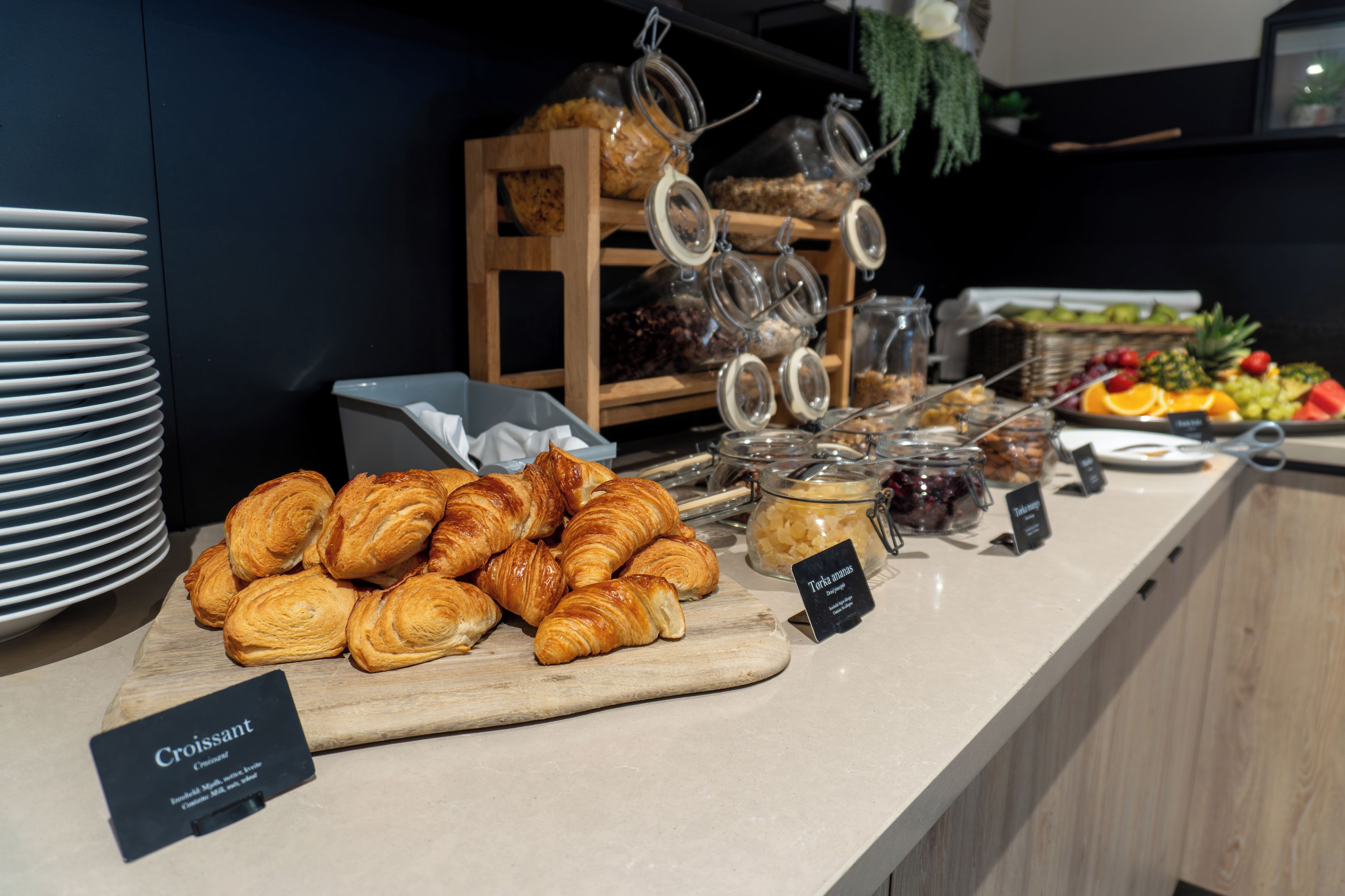 A breakfast buffet with croissants, fruits, and various condiments.