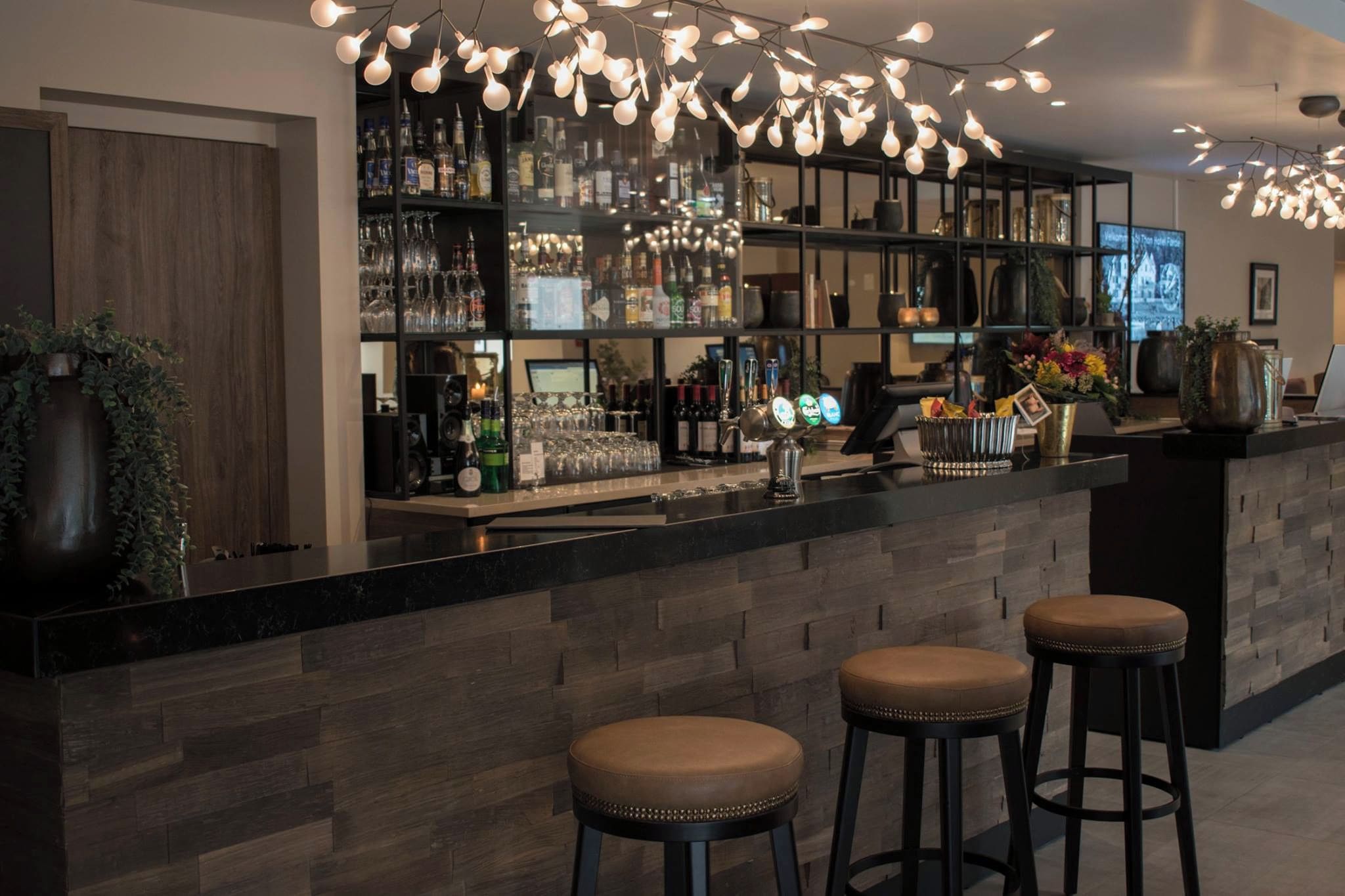 A bar area with a counter, stools, shelves with bottles, and a unique light fixture.