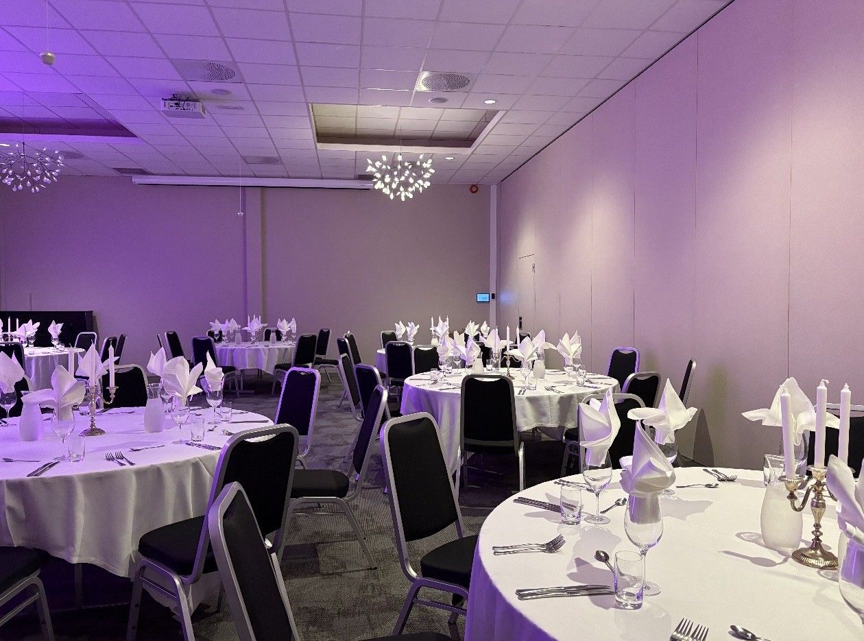 Un salón de banquetes con mesas redondas, sillas y manteles blancos.